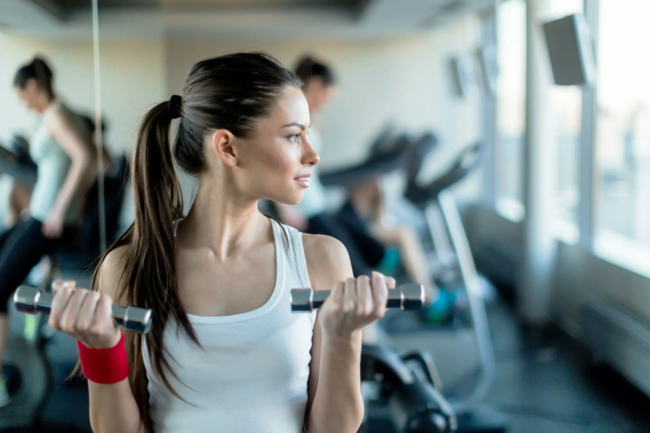 Young woman lifting dumbbell in gym, focused on workout.