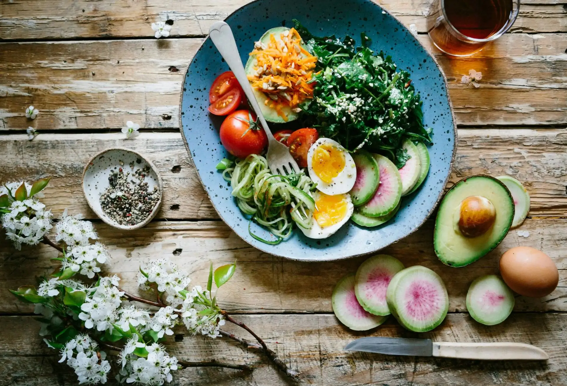 A colorful breakfast bowl with eggs, avocado, and vegetables on a wooden table.